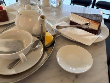 Beyaz tabakta bir parça çikolatalı kek, çay poşeti ve çaydanlık, yanında limon, kafede tatlı tatlı tatlı, kenar görüş, seçici odaklanma.