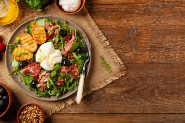 Salad with burrata cheese and croutons. Wooden background.