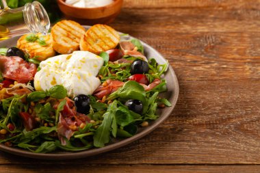Salad with burrata cheese and croutons. Wooden background.