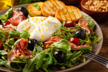 Salad with burrata cheese and croutons. Wooden background.