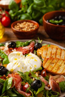Salad with burrata cheese and croutons. Wooden background.