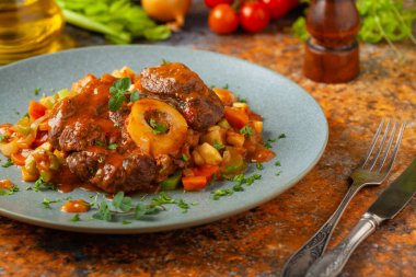 Ossobuco haşlanmış sebzelerle servis edilir. Renkli bir geçmiş. Gri tabak.