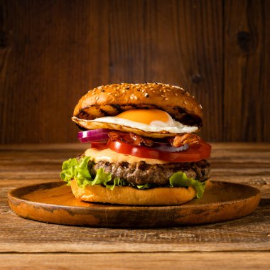 Kızarmış yumurtalı sığır burger. Tahta, doğal arka plan. Koyu stil.