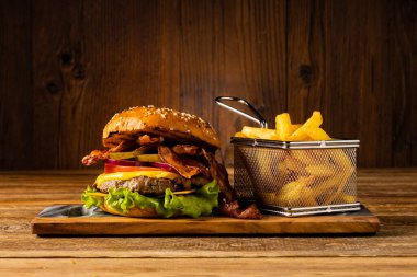 Pastırmalı klasik sığır burger. Patates kızartmasıyla servis edilmiş. Tahta, doğal arka plan. Koyu stil. 