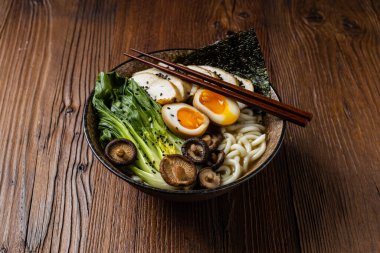 Traditional ramen with jerked pork or chicken.  With udon or ramen noodles. Served in classic bowls. Gyoza dumplings and mushrooms in the background.  Natural wooden background. clipart