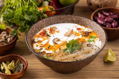 Tavuk, biber ve mantarlı Tayland çorbası. Hindistan cevizi sütüyle birlikte. Klasik bir Asya kâsesinde servis edilmiş. Arka planda doğal ahşap..