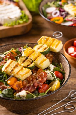 Izgara yemeklere domuz pastırması ve halloumi peynirli lezzetli salata eklendi. tahta arkaplan.