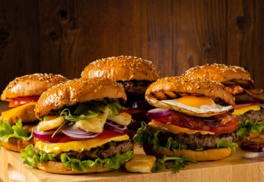 Kızarmış yumurta, pastırma ve ızgara halloumi peynirli sığır eti ve tavuk burger. Tahta, doğal arka plan. Koyu stil.