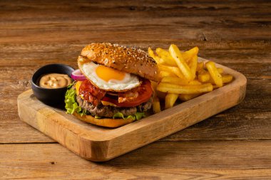 Kızarmış yumurtalı sığır burger. Patates kızartmasıyla servis edilmiş. Tahta, doğal arka plan. Koyu stil.