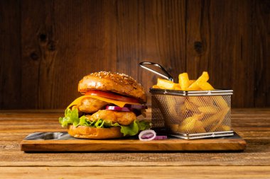 Tavuk çizburger. Patates kızartmasıyla servis edilmiş. Tahta, doğal arka plan. Koyu stil.