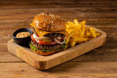 Klasik sığır burger. Patates kızartmasıyla servis edilmiş. Tahta, doğal arka plan. Koyu stil. 