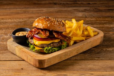 Pastırmalı klasik sığır burger. Patates kızartmasıyla servis edilmiş. Tahta, doğal arka plan. Koyu stil. 