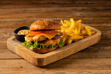 Tavuk çizburger. Patates kızartmasıyla servis edilmiş. Tahta, doğal arka plan. Koyu stil.