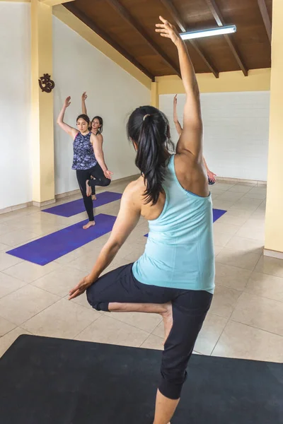 Yoga teacher with her back showing a standing yoga pose to her students in the yoga room