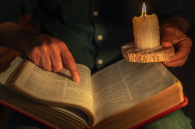 Unrecognizable man studying the bible pointing to bible passage lighting up with a candle