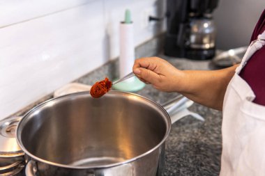 Unrecognizable woman in apron placing achiote in a pot. High quality photo
