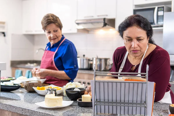 A mature woman and her elderly mother cooking following a recipe in a book in the kitchen. High quality photo