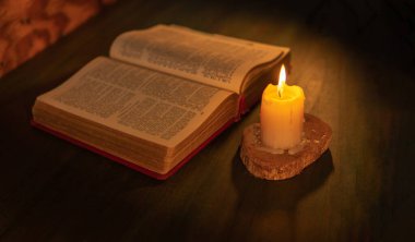 Ahşap bir masanın üzerindeki mum ışığıyla aydınlatılmış İncil. dini arkaplan