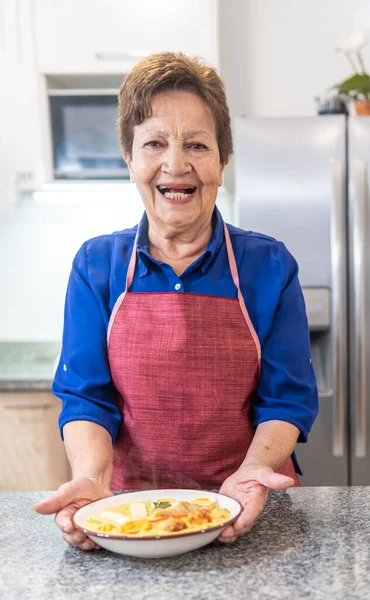 smiling older adult woman offering a plate of fanesca looking at the camera. High quality photo