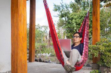 Hamakta dizüstü bilgisayarıyla çalışan Latin bir adam. Yüksek kalite fotoğraf