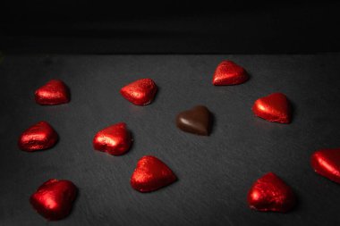 Kırmızı ambalajlı kalp şeklinde çikolatalar. Bir tanesinin siyah arka planında fotokopi alanı olan bir ambalajı yok. Çikolata aşkı konsepti