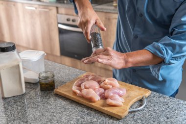 Tanınmayan bir adam mutfakta pişirmek için tavuk göğsünü biberle tatlandırıyor.