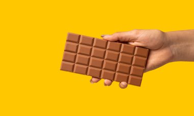 Sarı arka planda dikdörtgen çikolatalı bir kadın eli.