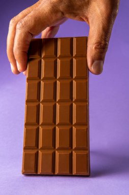 Mor arka plana çikolata yerleştiren bir adamın elini yakın plan çek. Dikey fotoğrafçılık