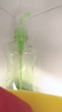 Avokado sabununu süngerin üzerine koyan kırmızı eldivenli bir elin yakın çekimi. Dikey video