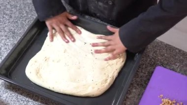 Mutfaktaki yemek tepsisine ekmek hamuru koyan tanınmayan bir kadının ellerinin tepe üstü görüntüsü.