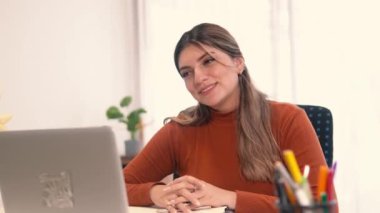 Genç bir Latin kadın video konferansı sırasında bilgisayarını kullanarak neşeyle gülümsüyor.