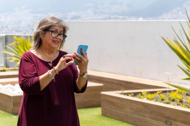 Üst düzey Latin kadın sabah bahçede gülümseyen cep telefonuna bakıyor.
