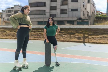 İki arkadaş, biri protez bacaklı ve kaykaylı, diğeri de patenli, güneşli bir günün tadını çıkarıyorlar.