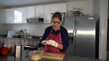 Eldiven giyen yaşlı bir kadın muz soyar ve tahta kesme tahtasında muz hazırlar.