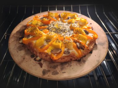 Sarı ve turuncu dolmalık biberli, mantarlı ve peynirli ev yapımı bir pizza fırında bir pizza..