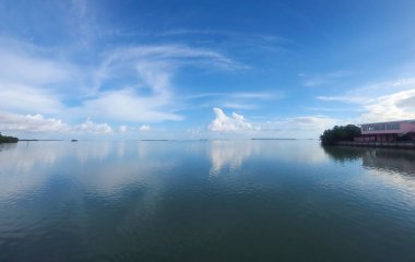 Durgun suları ile Florida Everglades deniz manzarası mavi gökyüzünü yansıtıyor ve ufuk üzerinde küçük adalar olan dağınık bulutlar.