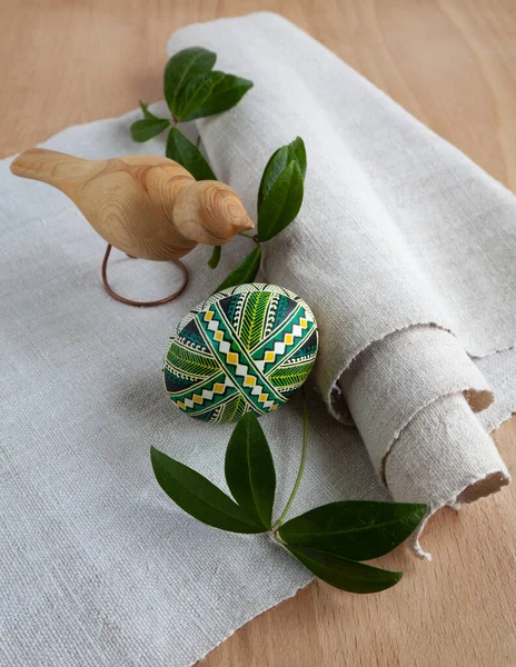 A green Easter egg and a wooden bird on a background of linen fabric