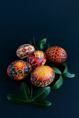 handmade Easter eggs in warm colors with a branch of periwinkle on a black background