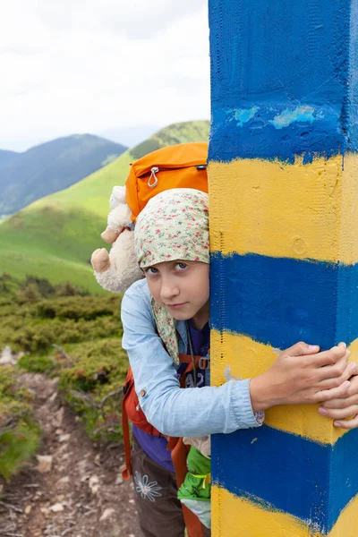 A girl with a backpack and a toy hugs a border post on the Ukrainian border in the mountains