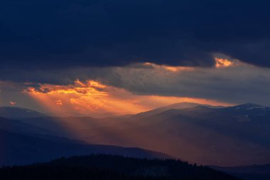 Güneş ışınları dağların üzerinde kara bulutlar arasında