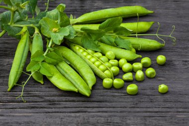 Koyu ahşap arka planda taze bezelye kabukları ve taneleri.