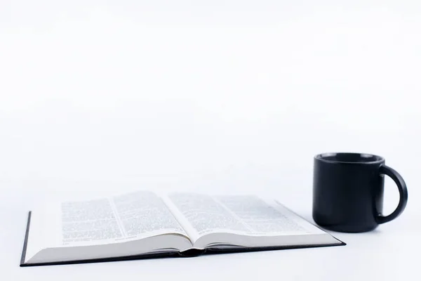 The Holy Bible is open. A cup and a book. On a white background.
