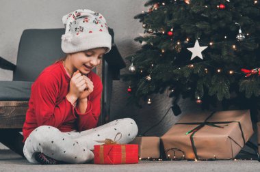 Hediye. Kırmızı pakette Noel ağacının altında bir hediye. Yılbaşı. Çocuklar hediyeleri açar.