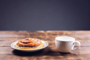Masada bir fincan kahve, tabakta bir çörek. Kahvaltıda. Ahşap bir arka planda