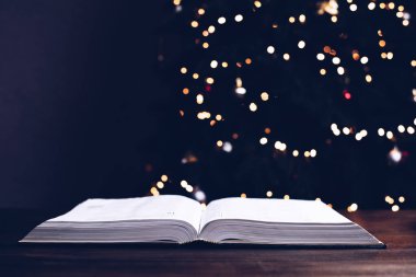 Masanın üzerinde açık bir İncil. Noel ağacının arka planında. Noel ayini. Çelenklerdeki Noel ağacı