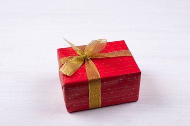 Hediye. Üzerinde altın fiyonk olan kırmızı bir paket. Beyaz bir arka planda. Noel ve Sevgililer Günü.