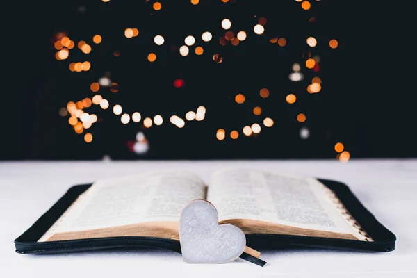 An open Bible on the table. The heart is a symbol of God\'s love for people. Prayer. On the background of the Christmas tree