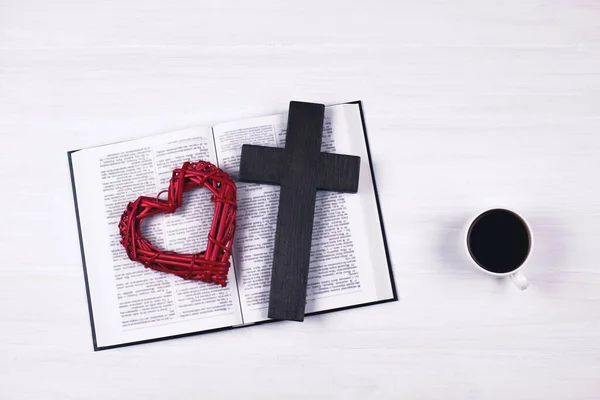 An open Bible on the table. The cross and heart are a symbol of God\'s love for people. Prayer