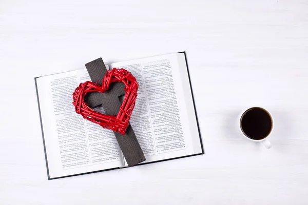 The Holy Bible is open. A cross and a red heart on a book. A cup of coffee on the table. A symbol of God\'s love and forgiveness. Prayer