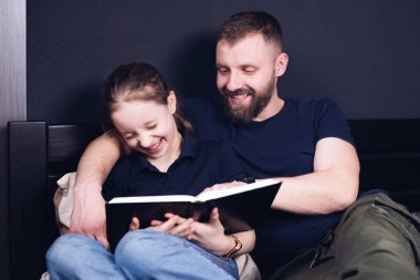 Baba ve kızı İncil 'i birlikte okuyorlar. - Aile. Mutlu bir çocuk yatakta otururken gülümsüyor..